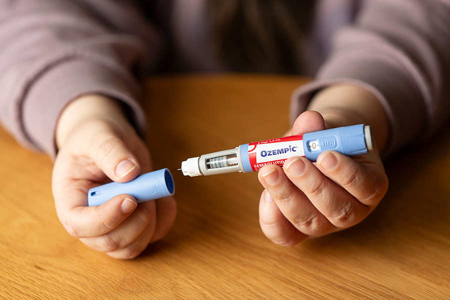 A person holds a light blue Ozempic pen, with the cap in one hand, and the pen in the other, with a needle on its tip.